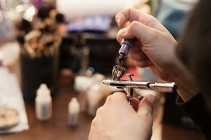 Hands of make up artist filling the airbrusher with liquid paint